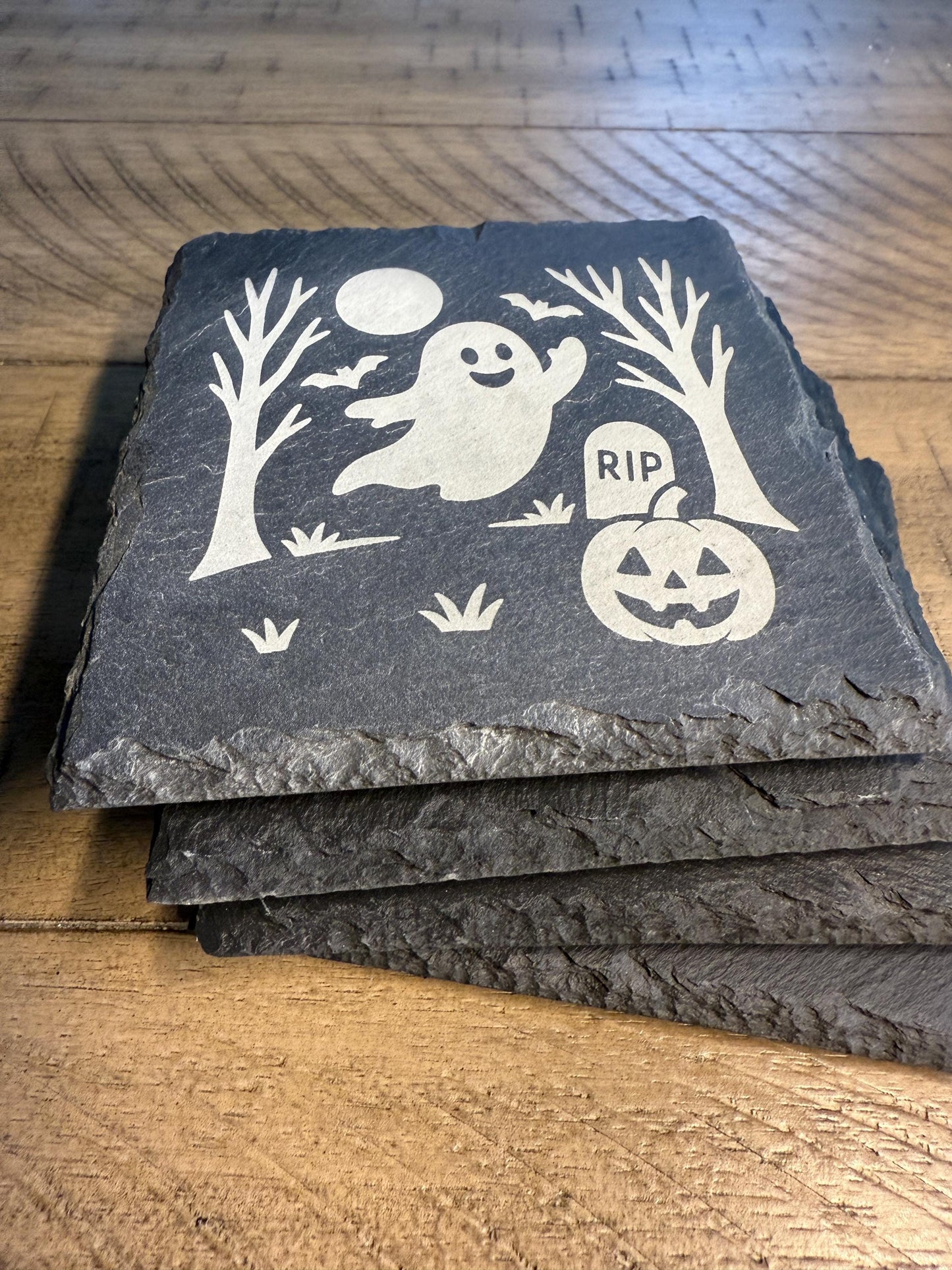 Set of slate coasters with Halloween designs on a wooden surface