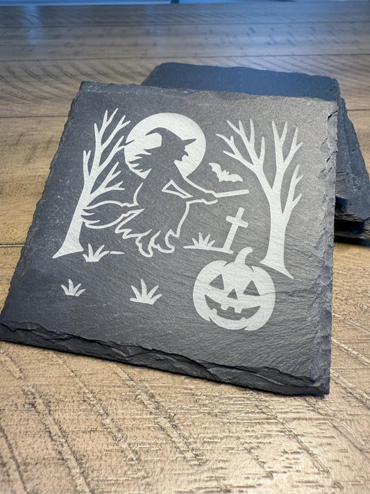 Slate coaster with Halloween design featuring a witch, pumpkin, and trees on a wooden surface.