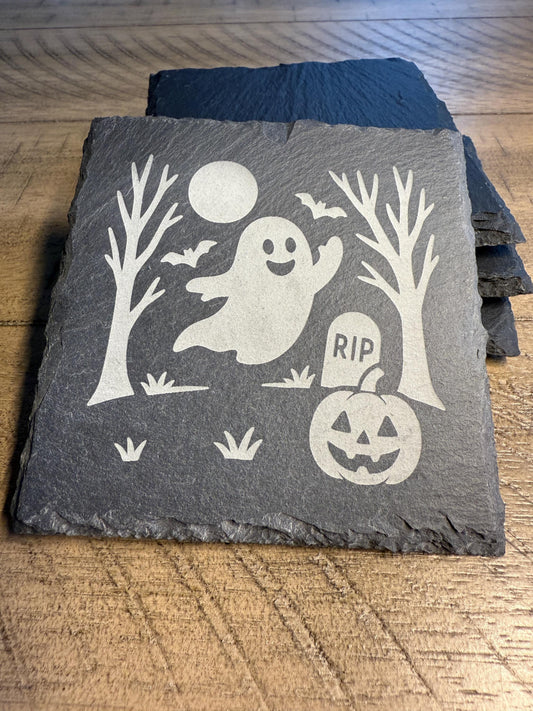 Slate coaster with Halloween design featuring a ghost, pumpkin, and tombstone on a wooden surface.