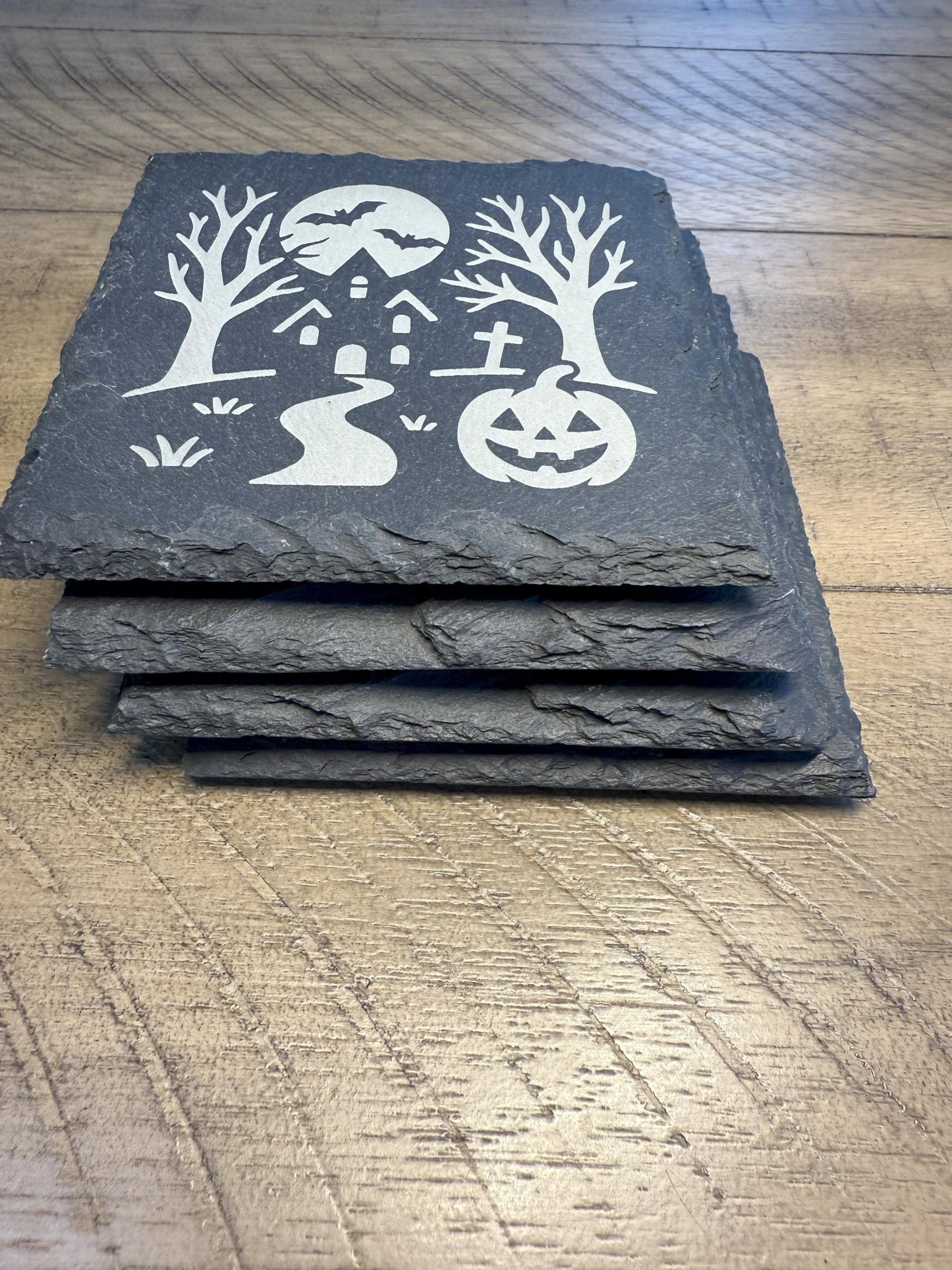 Set of four slate coasters with Halloween-themed designs on a wooden surface.