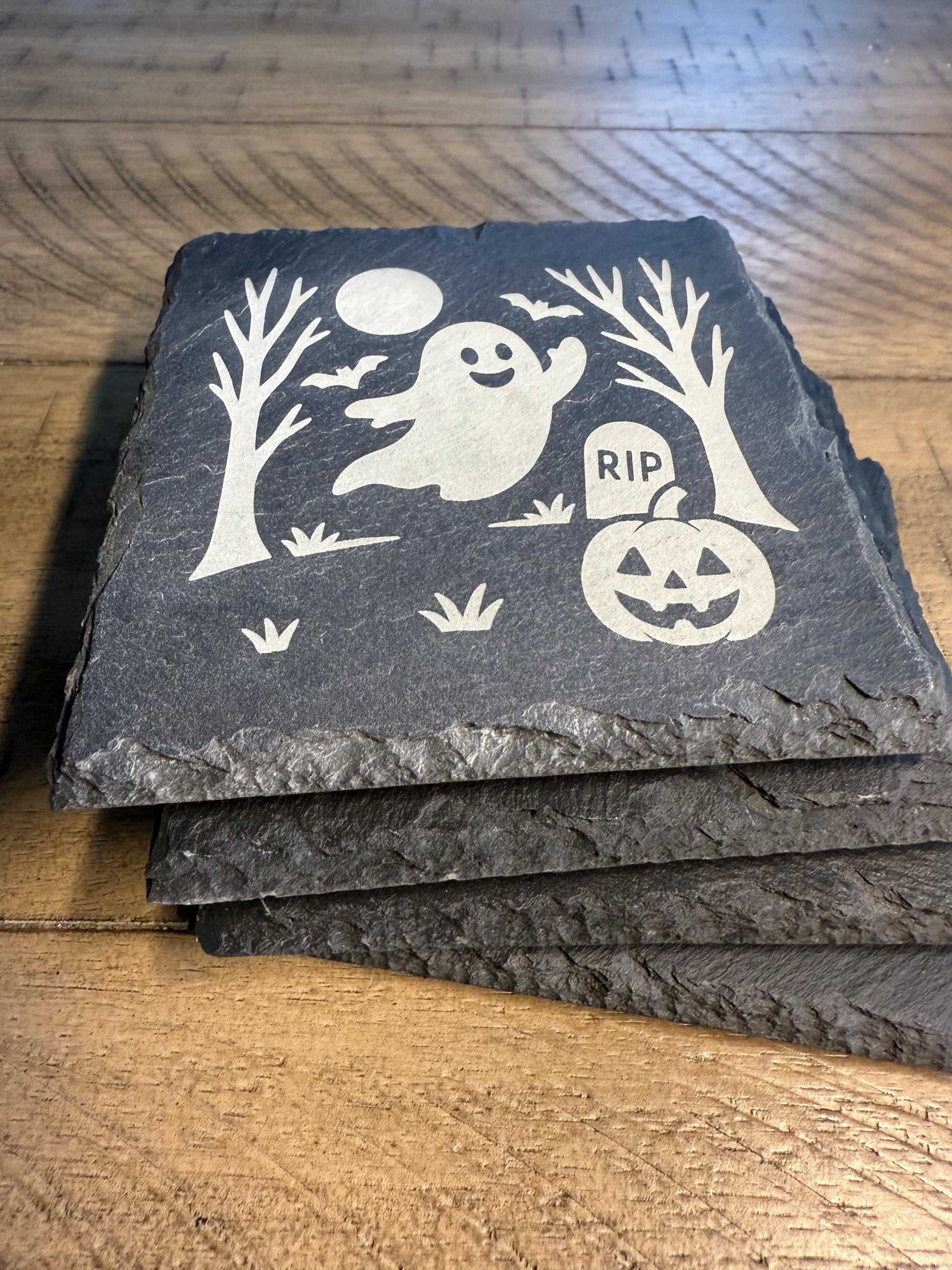 Set of slate coasters with Halloween designs on a wooden surface